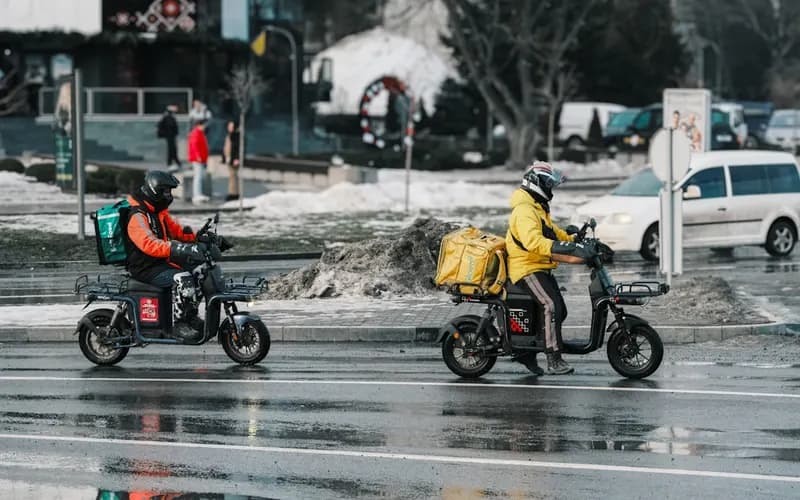 Two food delivery couriers on scooters on a city street